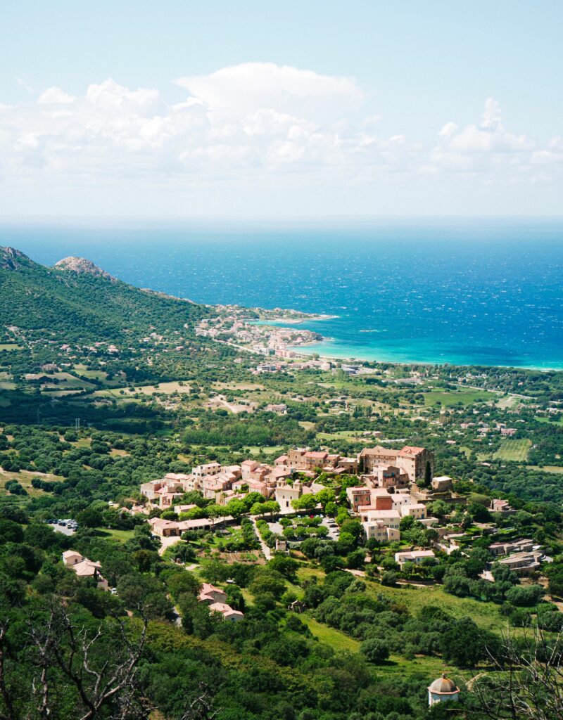 Stunning aerial view of Corsican coastline with lush greenery and azure sea, showcasing charming village.